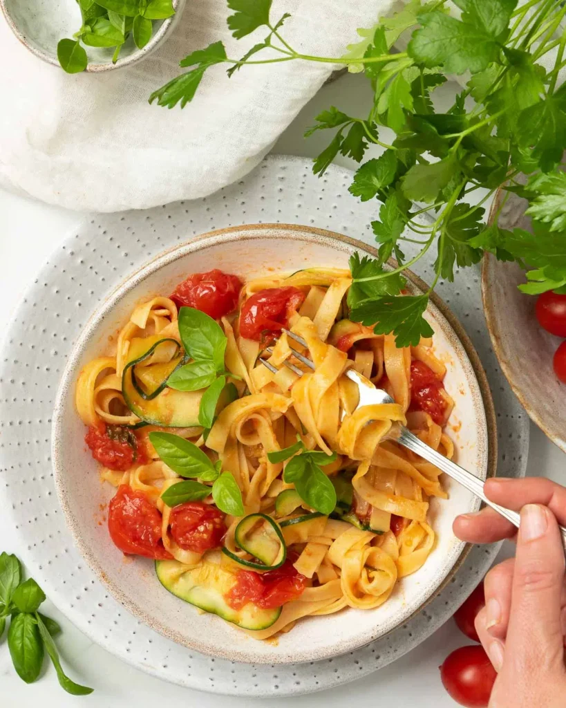 Tomato pasta dish topped with fresh herbs beside a bowl of fresh herbs and cherry tomatoes.