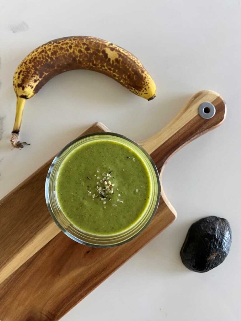 High potassium smoothie on a wood cutting board from a top down perspective beside a ripe banana and an avocado.