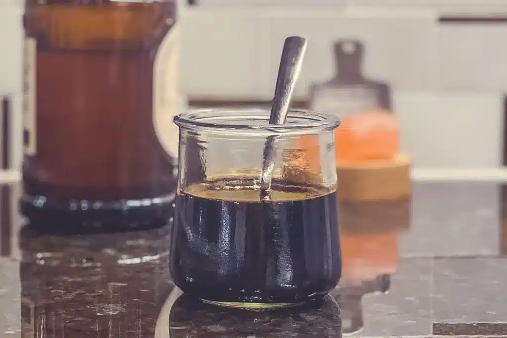Dark low sodium sauce in a clear jar with a spoon in it, beside a pepper grinder.