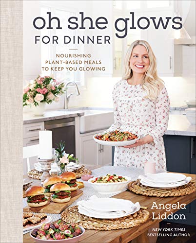 Oh she glows plant based book cover with a picture of Angela holding a plate of food in front of a table full of food.