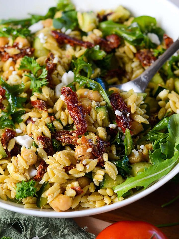 Low sodium orzo pasta with sundried tomato, goat cheese and arugula in a close up picture with a fork digging into the dish.