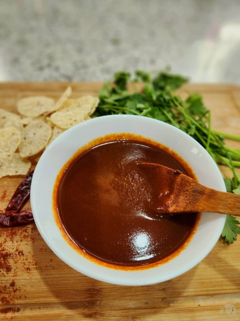 Low sodium enchilada sauce in a white bowl atop a wooden cutting board. Pictured with tortilla chips and fresh cilantro.