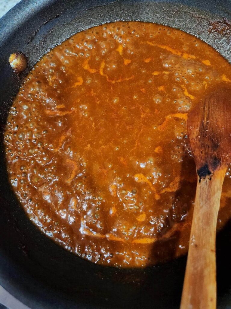 A pan with low sodium enchilada sauce cooking on the stove top. A wooden spoon is resting on the pan.