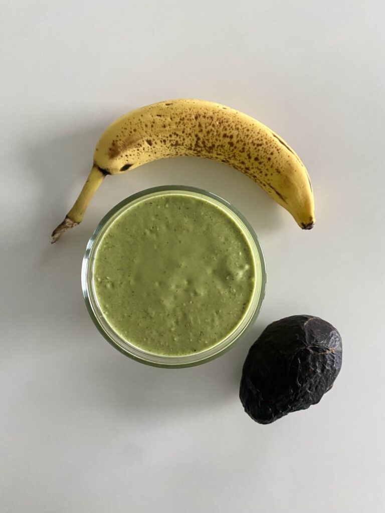 Green magnesium shake from top down perspective beside a full banana and avocado.