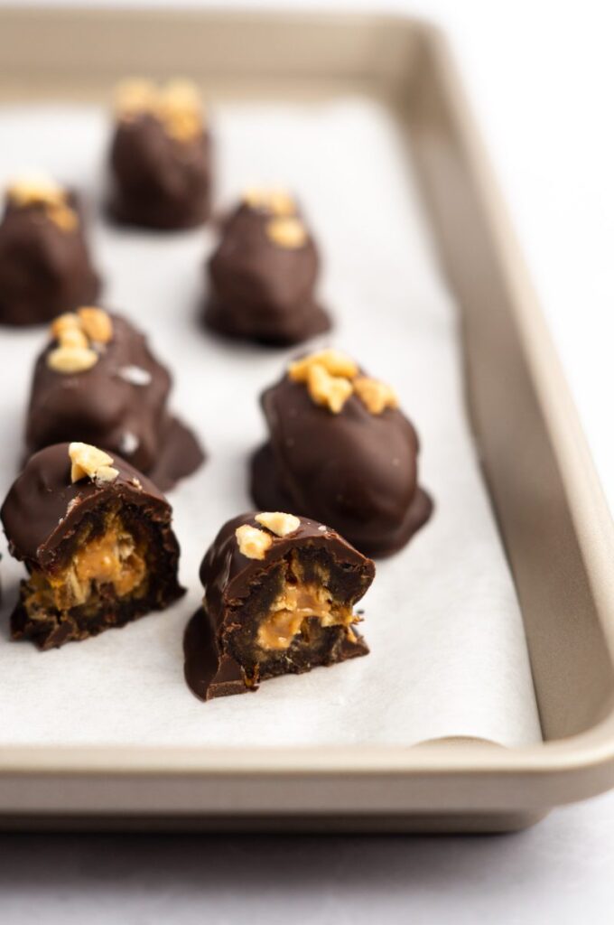 A baking sheet lined with parchment paper topped with low cholesterol desserts of chocolate balls topped with peanuts.