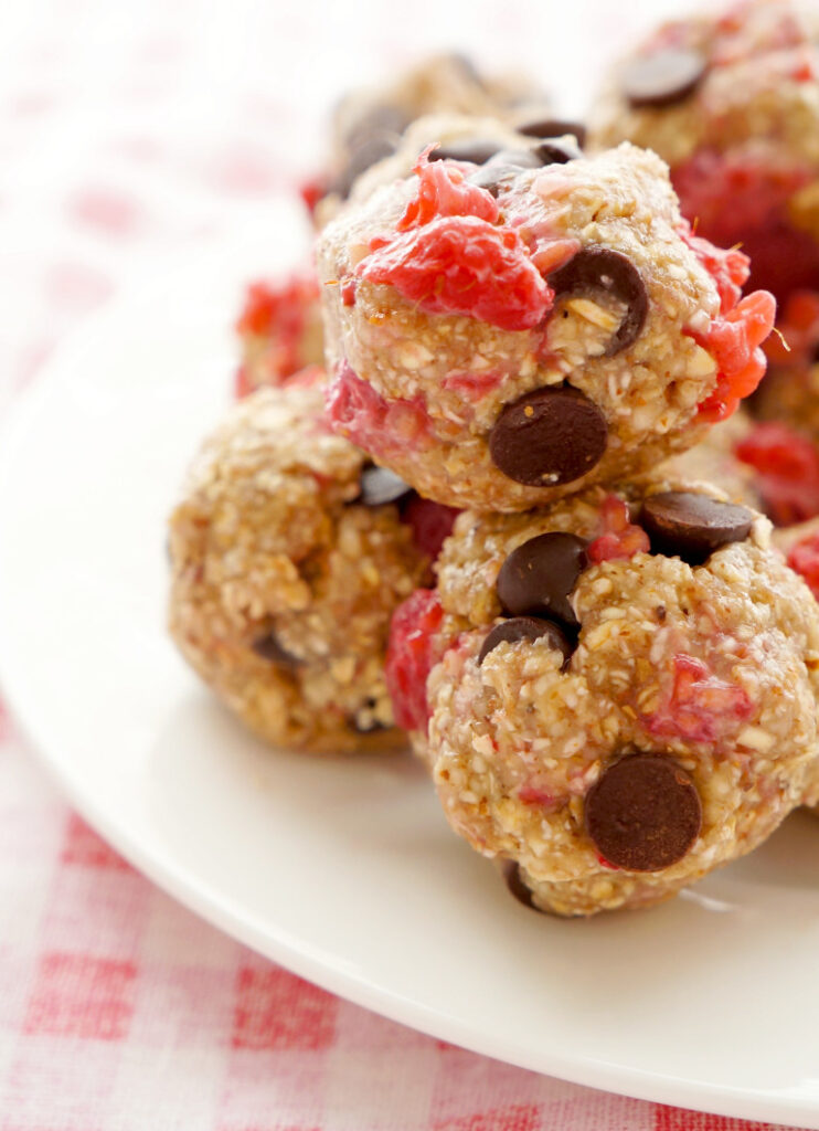 Raspberry chocolate oat balls is a low cholesterol dessert. These balls are stacked on a white plate on a red and white checkered table cloth.