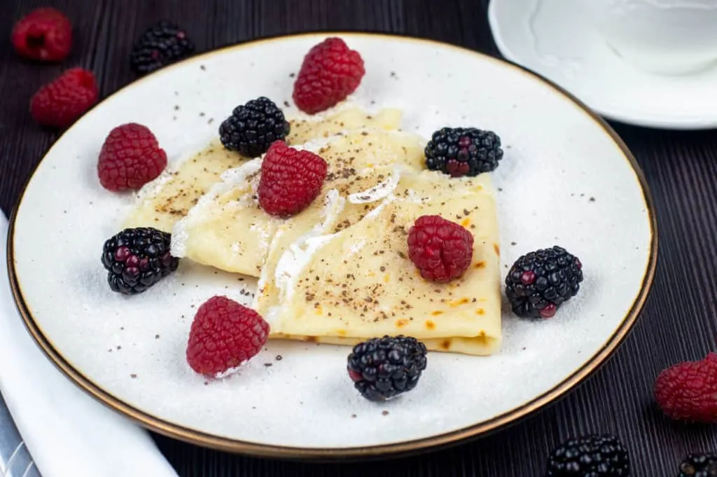 Low cholesterol desserts of 3 vegan crepes on a white plate topped with raspberries and blackberries.