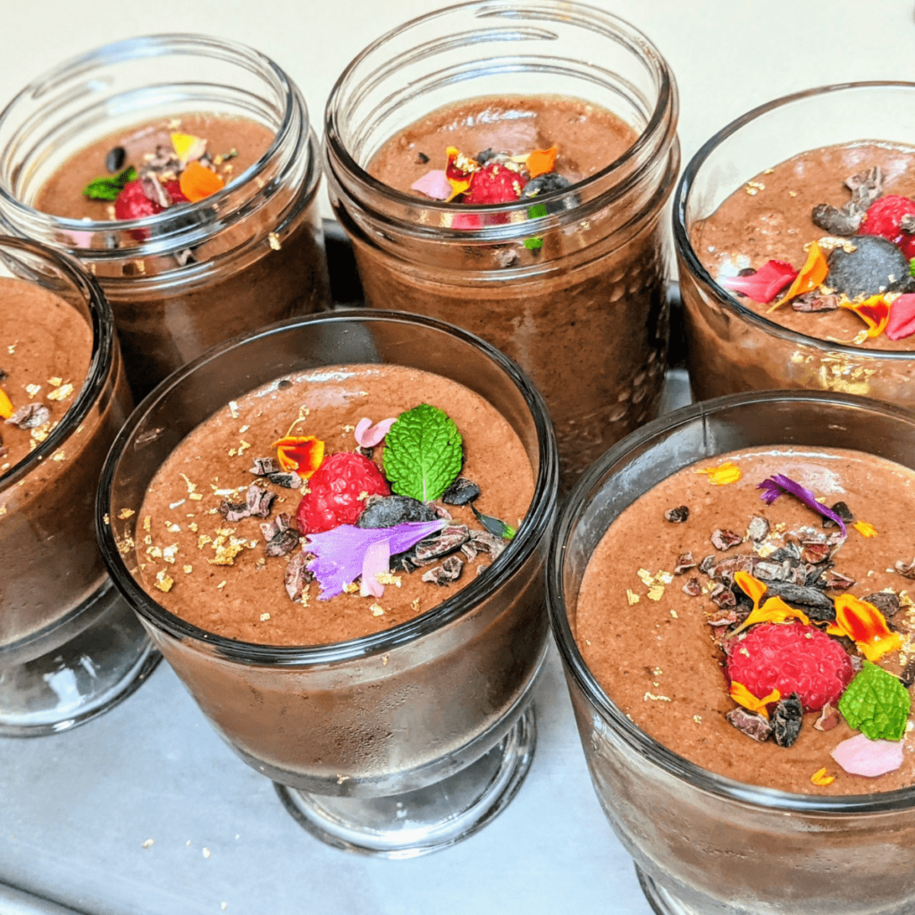 Six glass containers with a low cholesterol dessert of chocolate pudding topped with chopped chocolate bars.