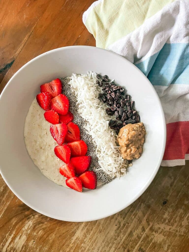 oatmeal in a white bowl with strawberries, peanut butter, coconut flakes and cocoa nibs.