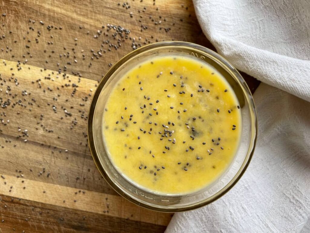 Homemade juice to lower cholesterol pictured in a glass atop a wood countertop and a white tea towel. Chia seeds are atop the juice.