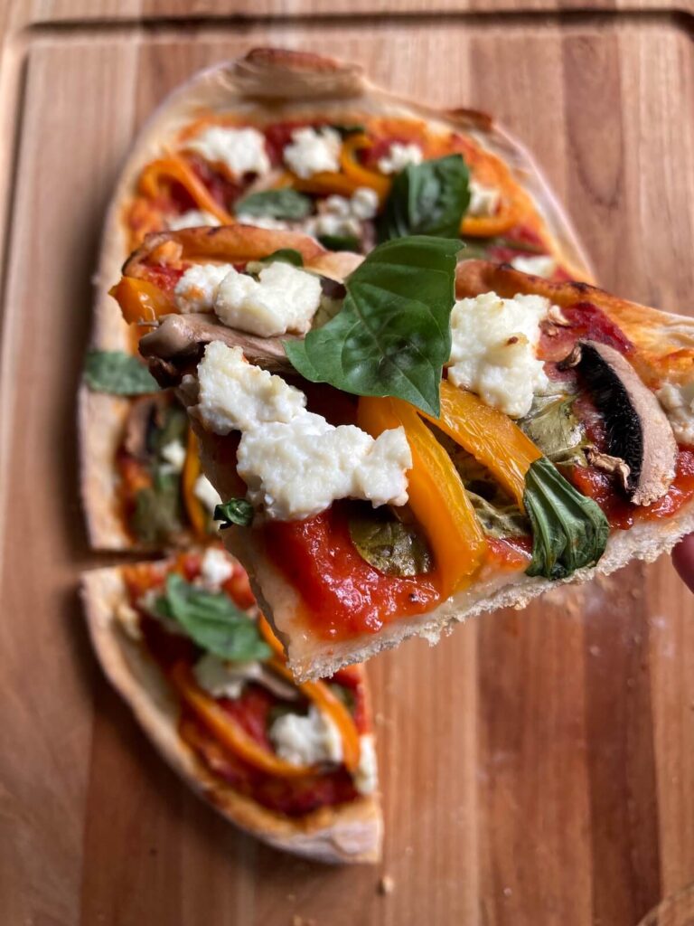 Close up image of a slice of low cholesterol pizza. The pizza is topped with spinach, tomato sauce, ricotta, bell pepper, and mushroom.