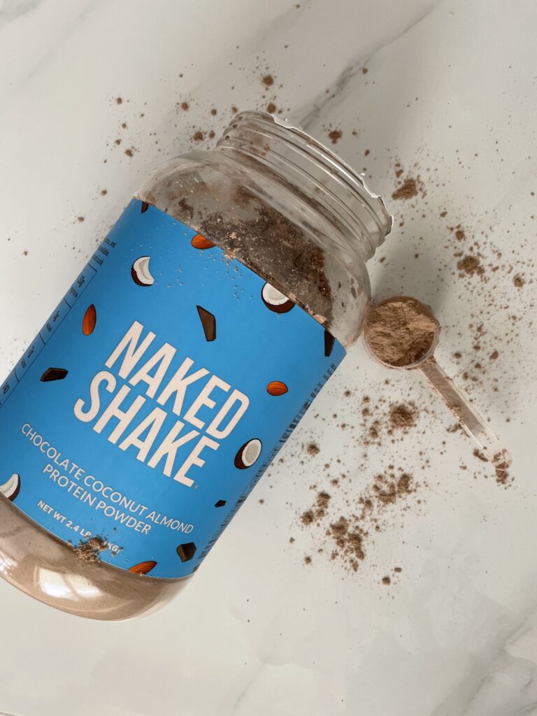 Blue naked shake low sodium protein powder container on white marble with protein powder sprinkled around it.