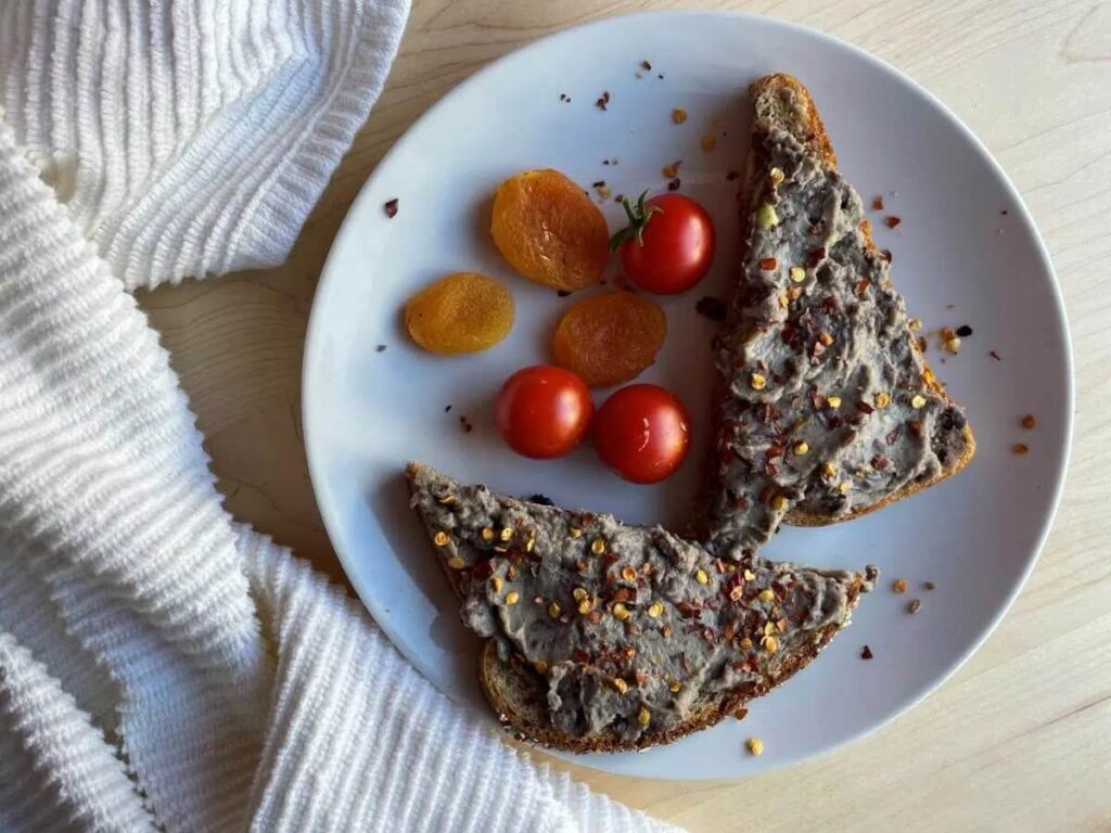 Black bean toast with tomatos and apricots, on a white plate and a white tea towel next to the plate.