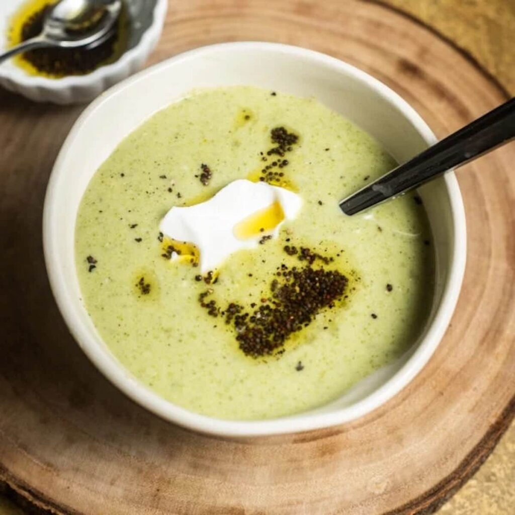 Broccoli almond soup pictured in a white bowl on top of a wooden surface.