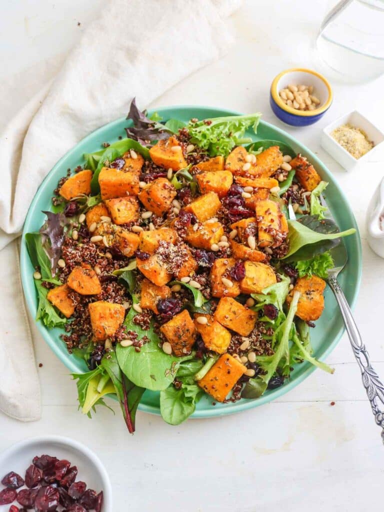 A butternut squash quinoa salad pictured in a turquoise dish with cranberries on the side.