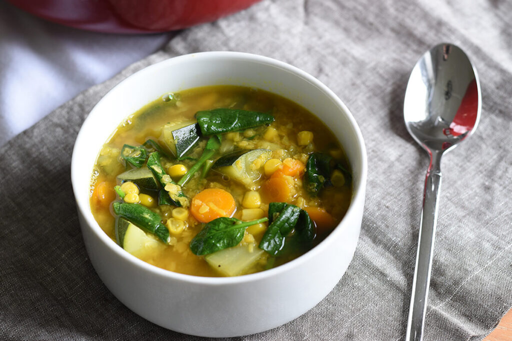 Lemon lentil soup in a white dish atop a grey towel with a spoon. 