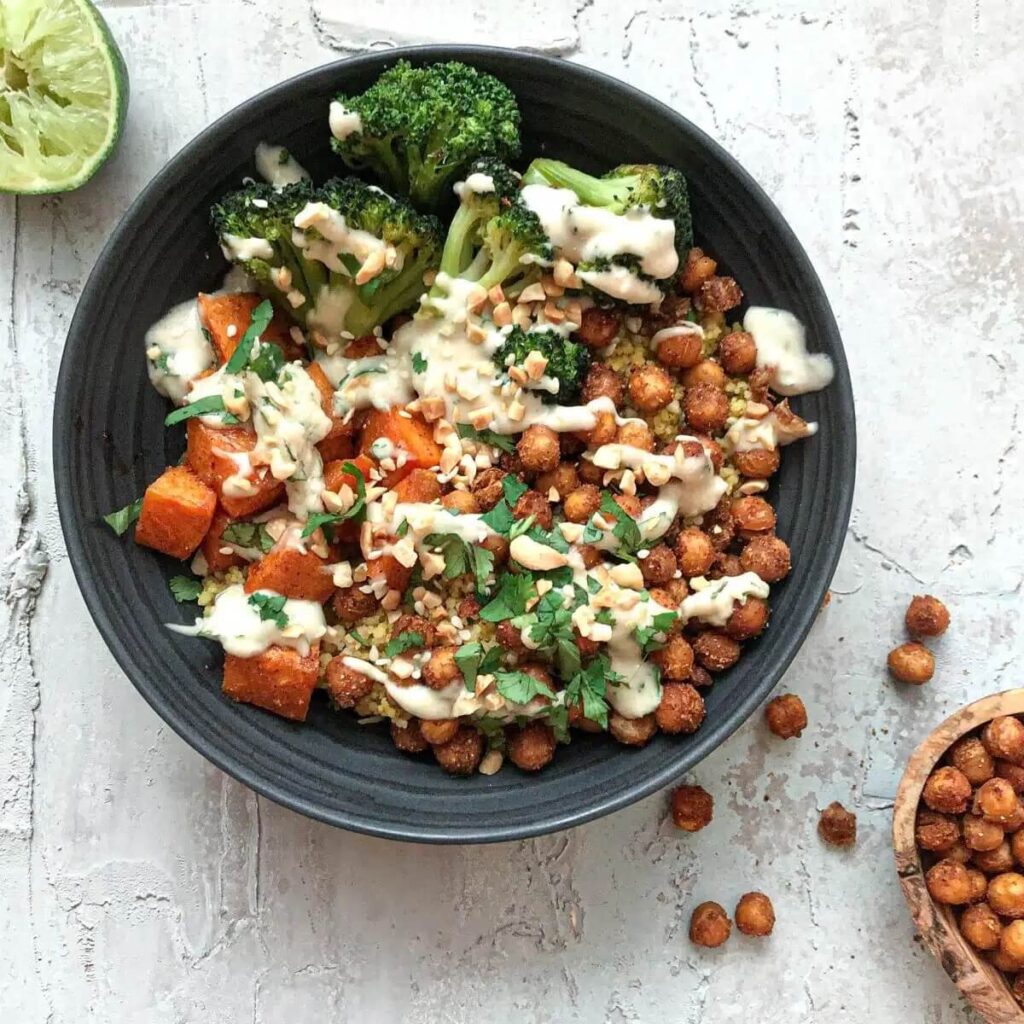 Mediterranean chickpea quinoa bowl in a dark grey dish, on a grey background with lime and seasoning chickpeas next to the dish.