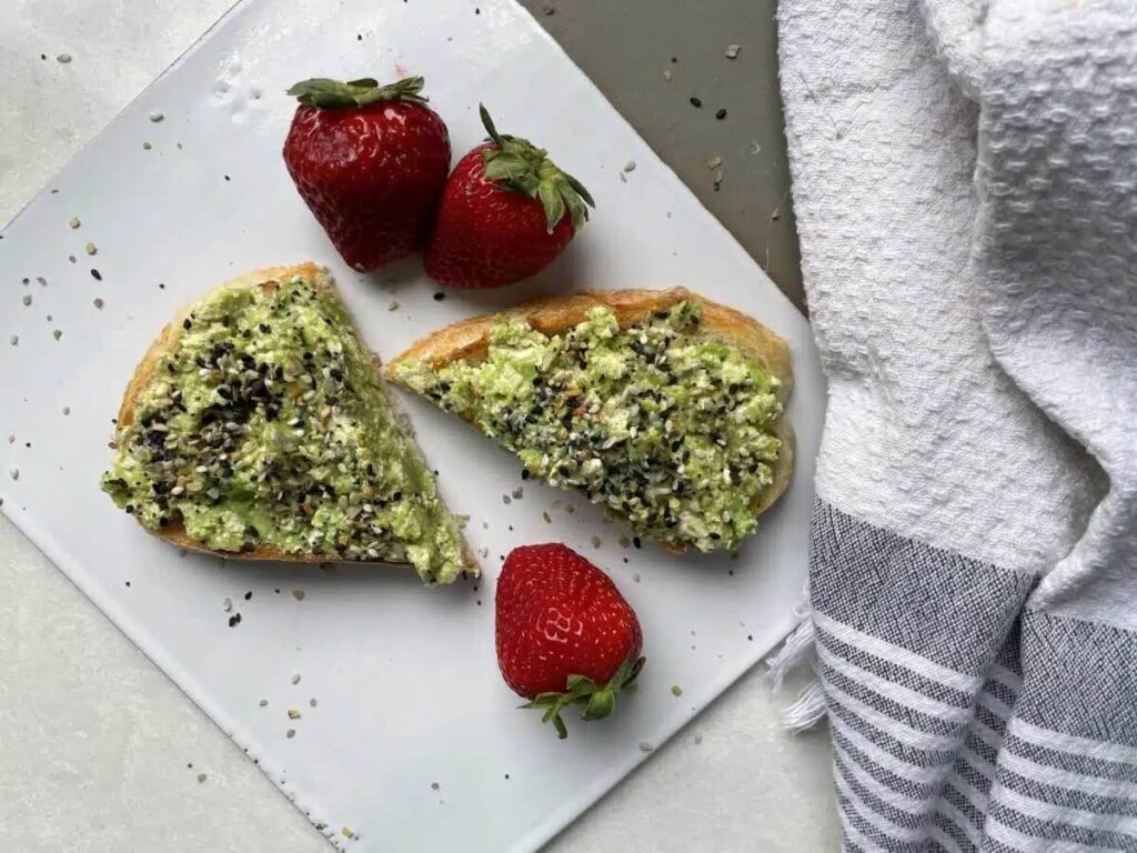 A slice of tofu toast on a white background with everything bagel seasoning and fresh strawberries.