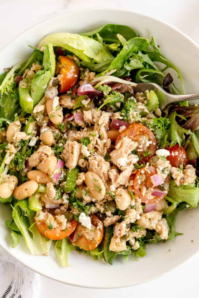 Salad in a white bowl with tuna, tomatoes, red onion, and white beans.