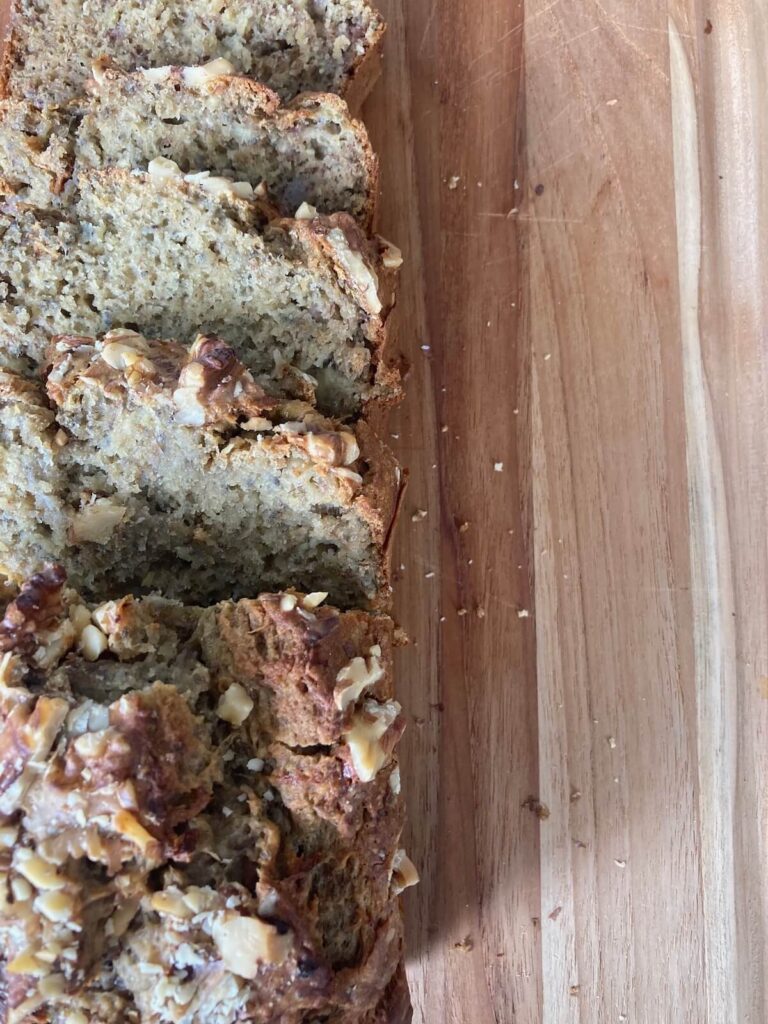 Chia seed banana bread on a wooden cutting board, sliced and topped with walnuts.
