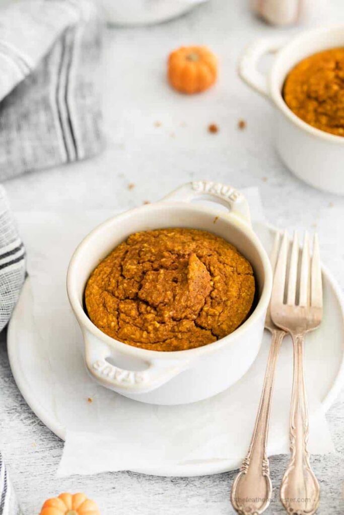 Pumpkin baked oats in a ramekin on top of a plate. On the plate is two forks. 