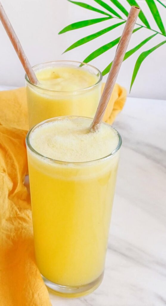 Two glasses with pineapple ginger juice, on a grey and white counter top.