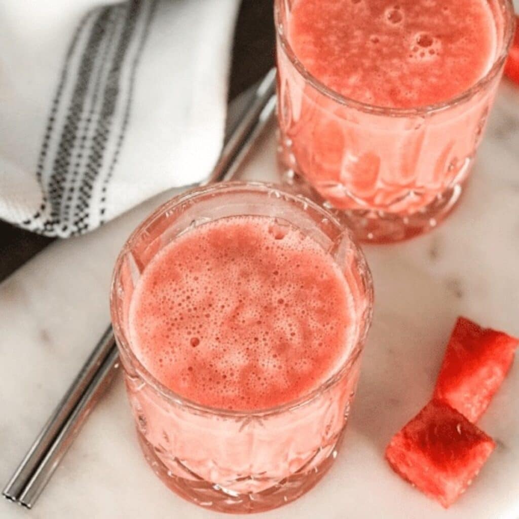 Two glasses with watermelon pineapple smoothie, and a tea towel and metal straw alongside the smoothies.