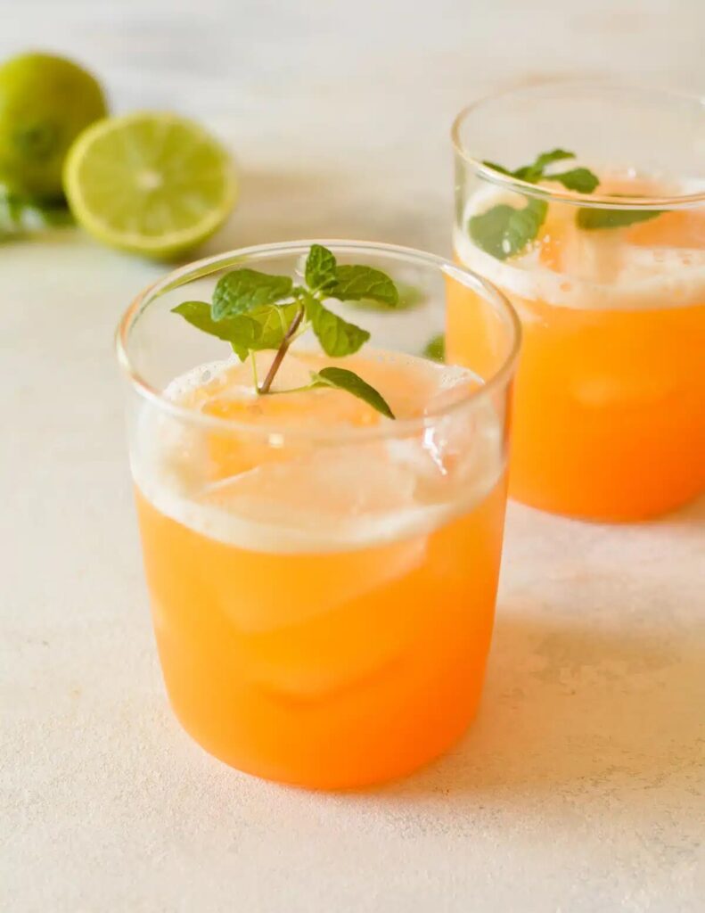 2 glass of cantaloupe juice topped with fresh herbs, and limes in the background. 