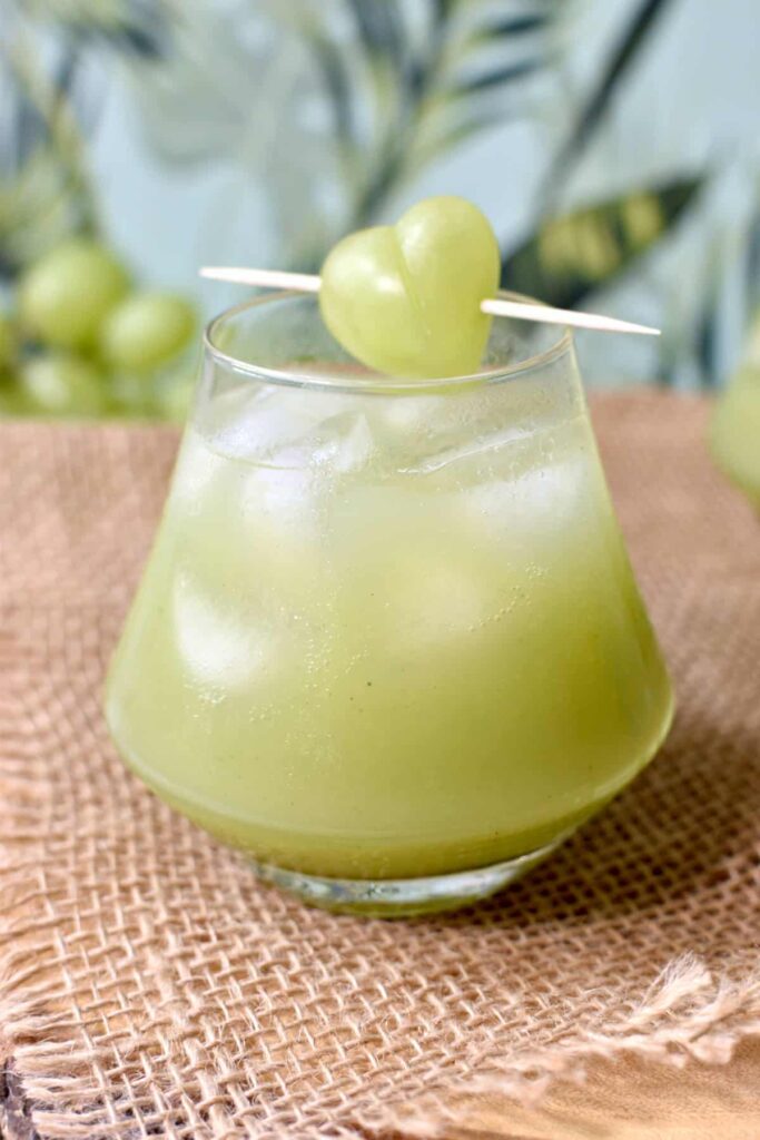Green grape juice in a glass, topped with a grape garnish. 