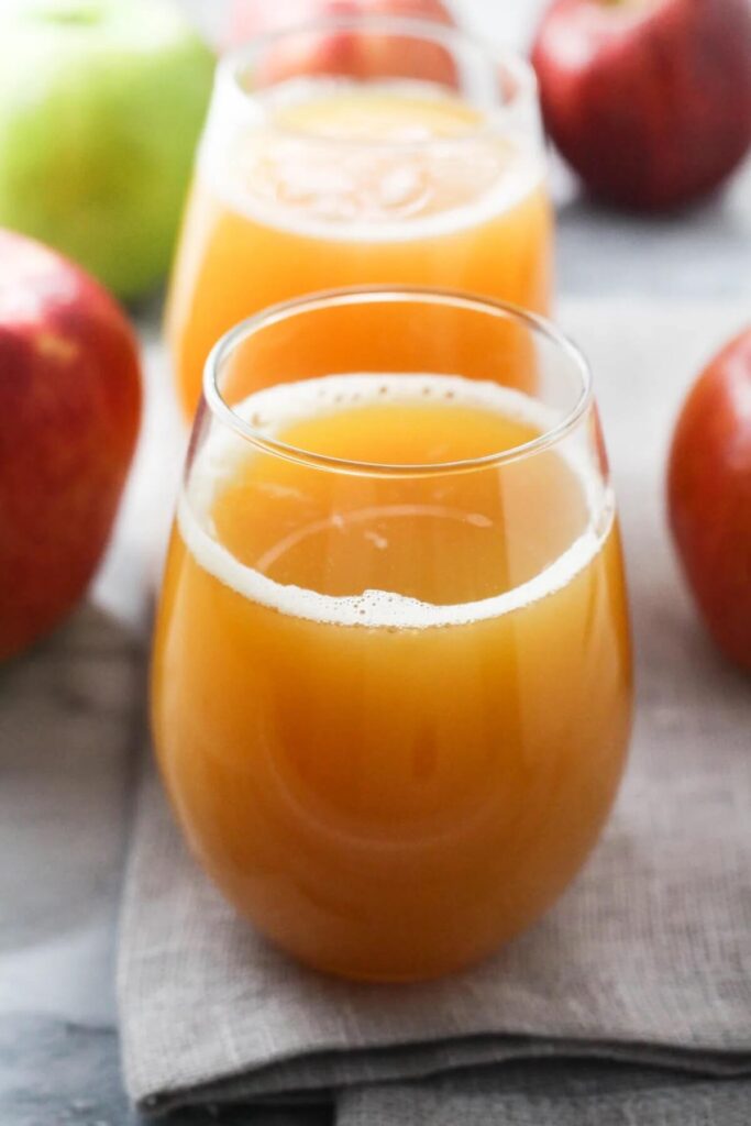 2 glasses of apple juice lined up. Apples are in the background. 