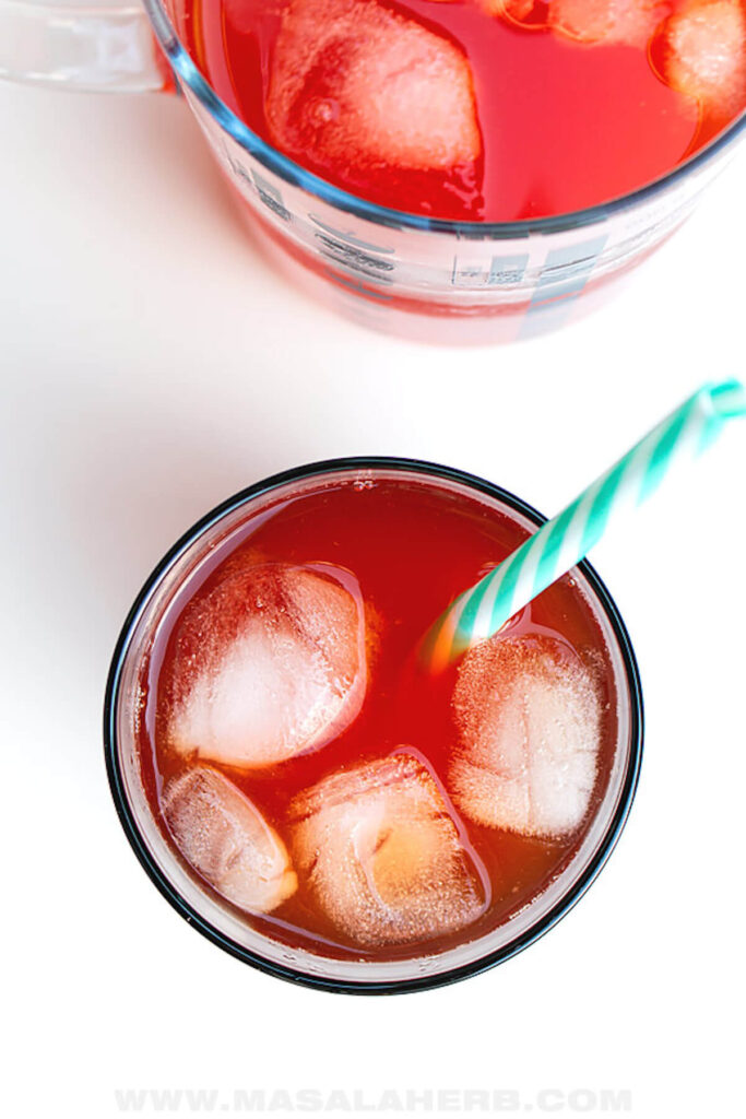 Two glasses of prickly pear juice pictured from above, served with ice in a glass and a blue and white striped straw. 