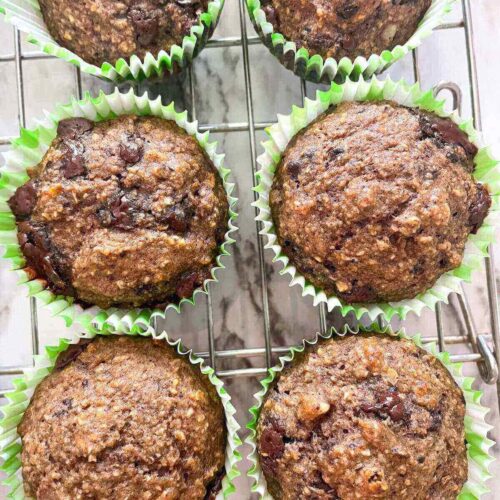 An image of low cholesterol muffins with banana and chocolate chips, pictured with white and green muffin liners on a cooling rack.