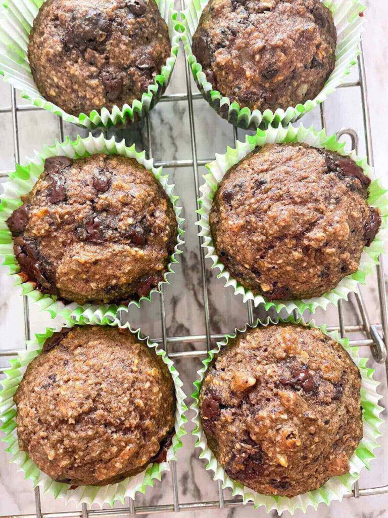 6 low cholesterol muffins with banana and chocolate chips in white and green muffin liners on a cooling rack. 