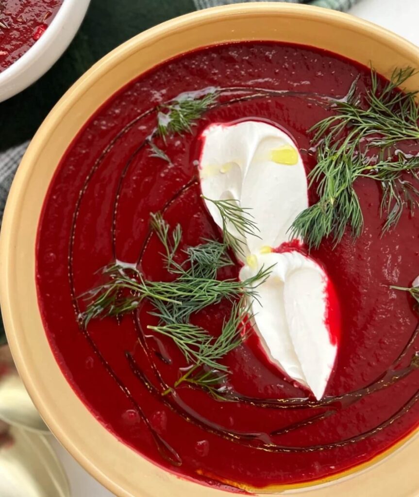 An image of Ukranian beet borscht in a yellow dish, topped with yogurt and fresh dill.