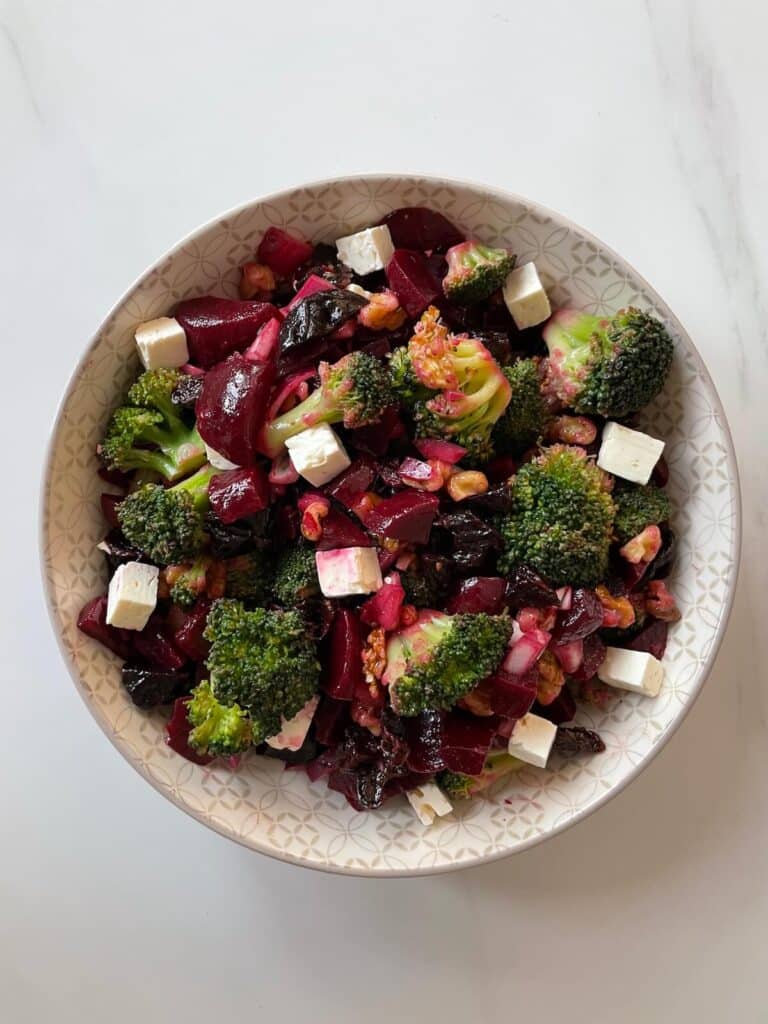 Beet and broccoli salad pictured in a white dish, on top of white and grey countertop.