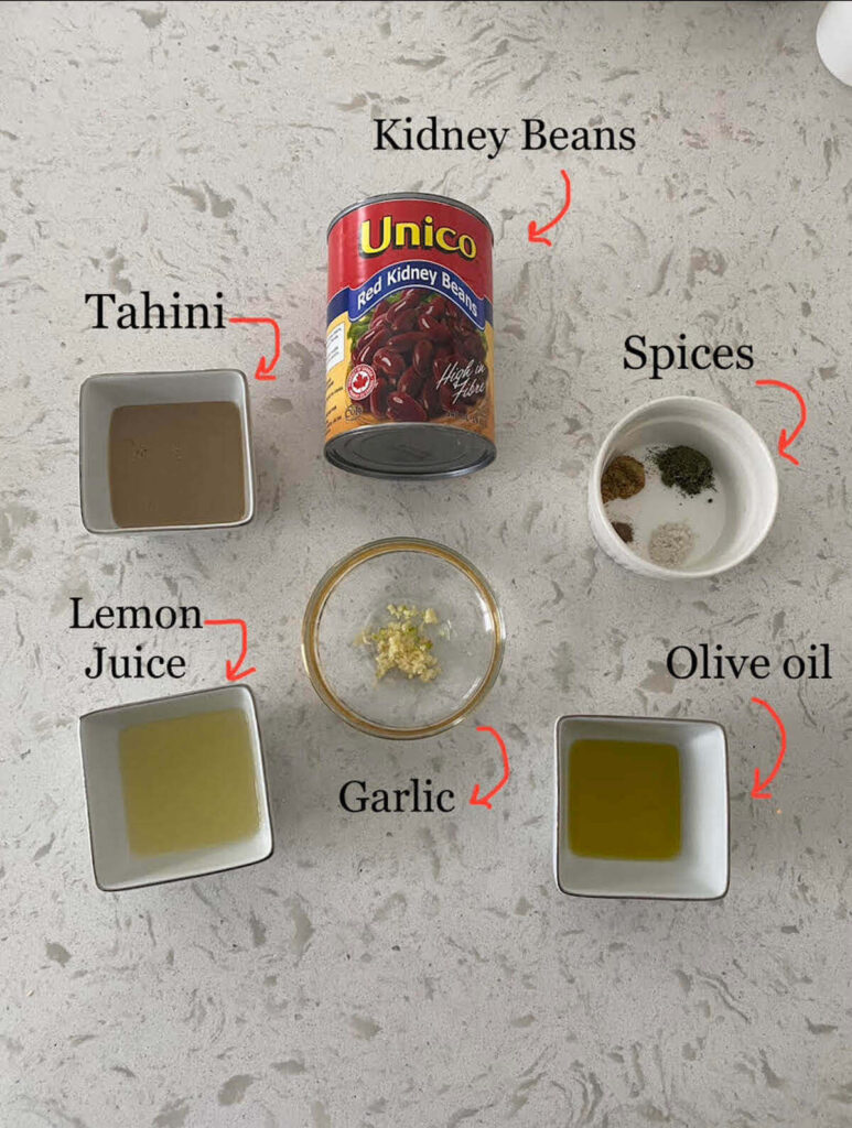 Ingredients for kidney bean hummus on a counter including kidney beans, lemon juice, tahini, olive oil, garlic, and spices.