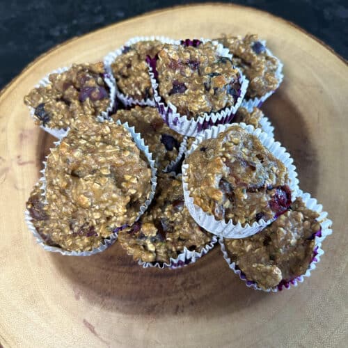 Healthy date blueberry muffins stacked and presented on a wood serving board with the wrapped on it.