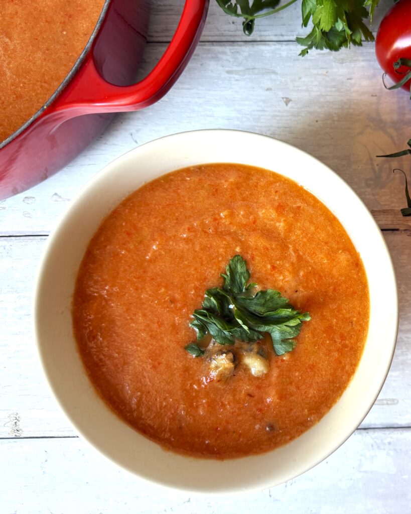 Blended soup in a white bowl on a white picnic table beside a red French filled with more soup.