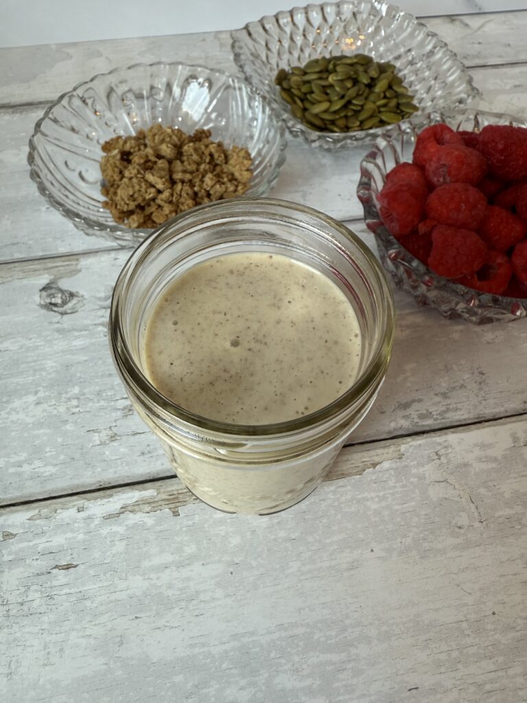 Blended overnight oats beside a bowl of granola, pumpkin seeds and fresh raspberries.