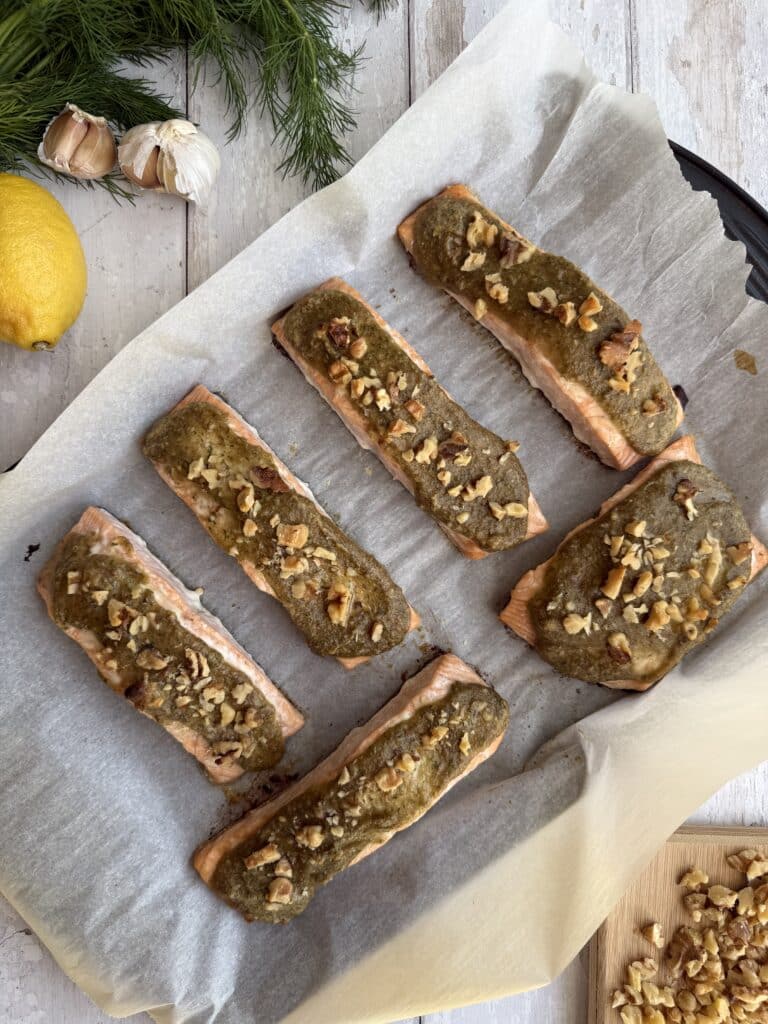 Walnut crusted salmon presented on parchment paper beside lemon, garlic, walnuts and dill.