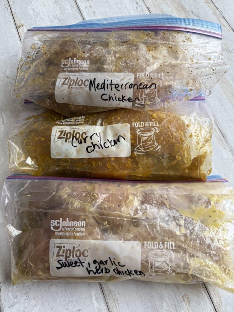 Three freezer friendly low sodium chicken marinades in separate ziplock bags on a wood table.