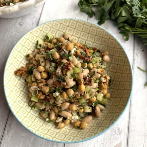 Low cholesterol bean salad displayed in a yellow bowl on a wood table beside parsley.