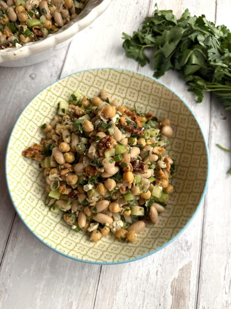 Low cholesterol bean salad displayed in a yellow bowl on a wood table beside parsley.