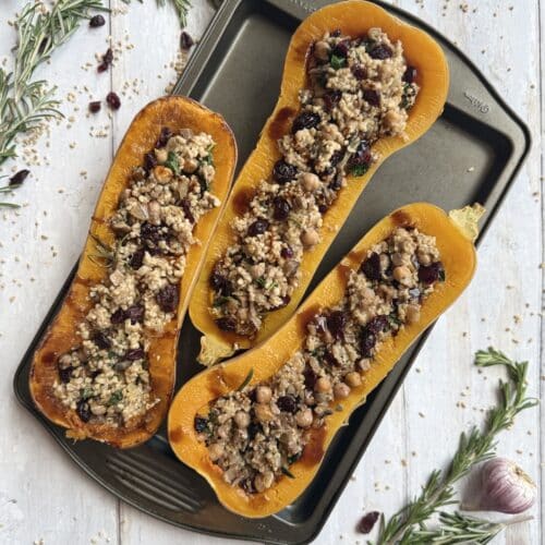 Oat Stuffed Butternut Squash (Low Cholesterol Side Dish) presented on sheet pan surrounded by rosemary and cranberry.
