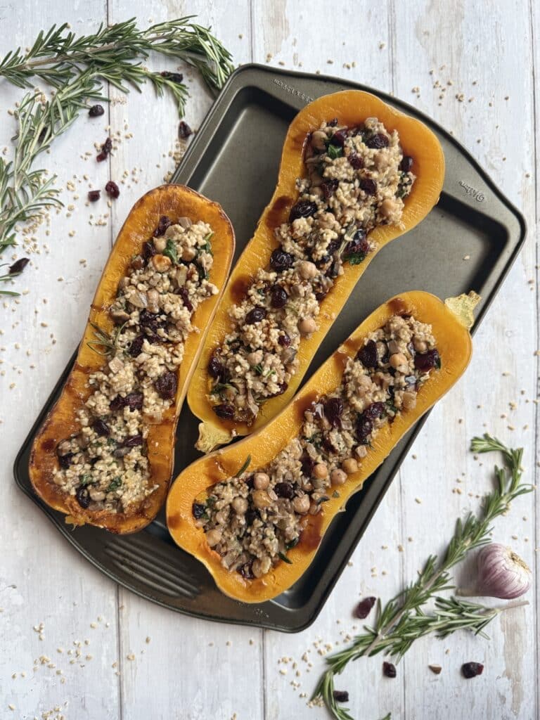 Oat Stuffed Butternut Squash (Low Cholesterol Side Dish) presented on sheet pan surrounded by rosemary and cranberry.